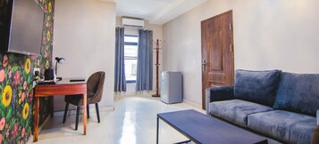 Una habitación con un sofá, un escritorio con silla, un televisor, un perchero y una puerta.