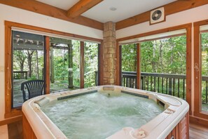 A hot tub in a wooden cabin with large windows and a stone pillar. - Galena Getaway w/ Hot Tub, Home Theater & More! (Galena)