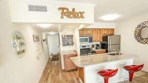 A modern kitchen with wooden cabinets, a stainless steel refrigerator, and a central island with red bar stools. - TAMPA CONDO (Tampa)