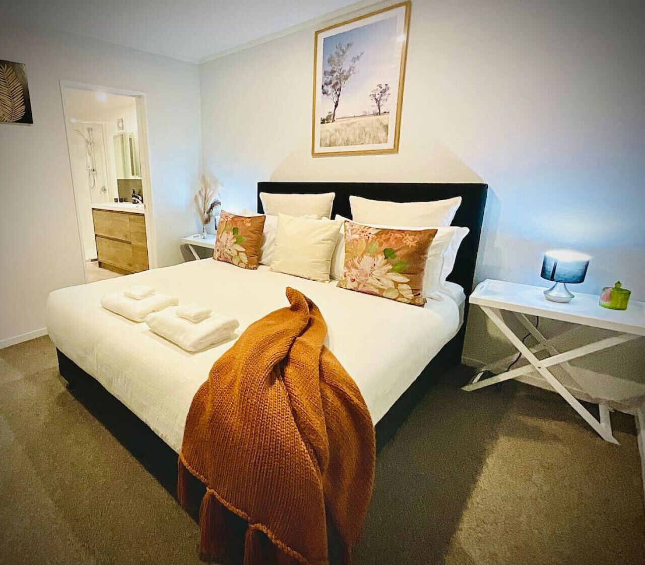 A neatly arranged bedroom with a bed, bedside tables, a nightstand, and a wall-mounted picture.