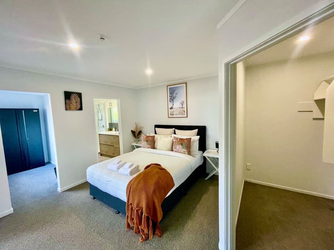 A bedroom with a bed, bedside tables, a nightstand, a mirror, and a door leading to another room.