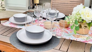Ett matbord dukat med tallrikar, glas och en vas med blommor, med en soffa och en tavla i bakgrunden.