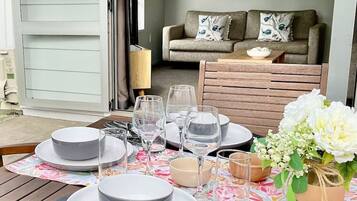 A dining table set with plates, glasses, and a vase of flowers, with a sofa and a painting in the background.
