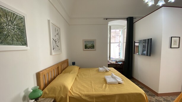 A hotel room with a bed, a desk, a chair, a TV, and artwork on the walls. - PROMOTION "TOURISTHOUSE MONOPOLI 10" ROOM1 TRIPLE WITH EN SUITE BATHROOM (MONOPOLI)