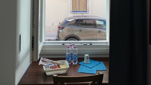 A room with a window overlooking a street. There is a table with a basket, bottles, and a cup. - PROMOTION "TOURISTHOUSE MONOPOLI 10" ROOM1 TRIPLE WITH EN SUITE BATHROOM (MONOPOLI)