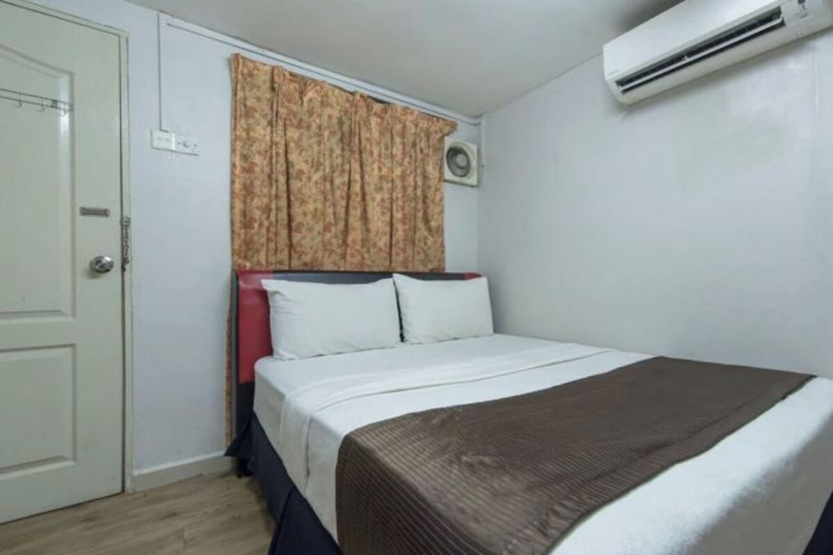 A hotel room with a bed, a window with curtains, an air conditioning unit, and a door.