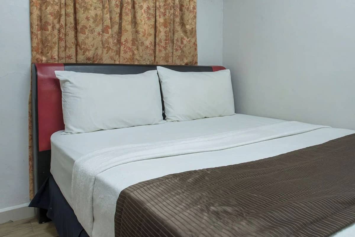 Una cama bien hecha con ropa blanca y una manta marrón, un cabecero rojo y una cortina con estampado floral.