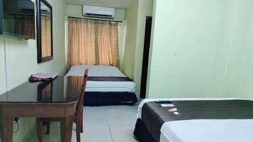 A hotel room with two beds, a desk, a chair, a TV, and an air conditioner.