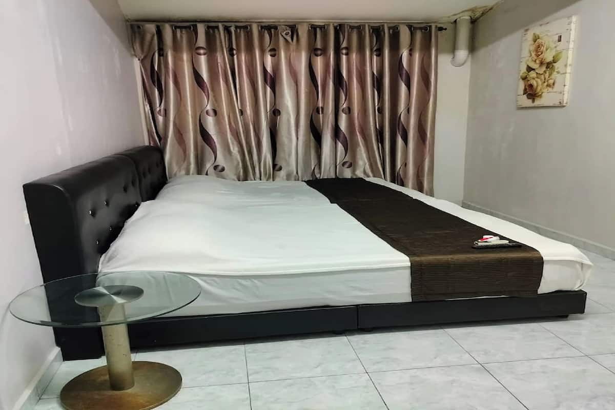 Una cama bien hecha con cabecera negra, una mesa de vidrio con base metálica y una cortina estampada.