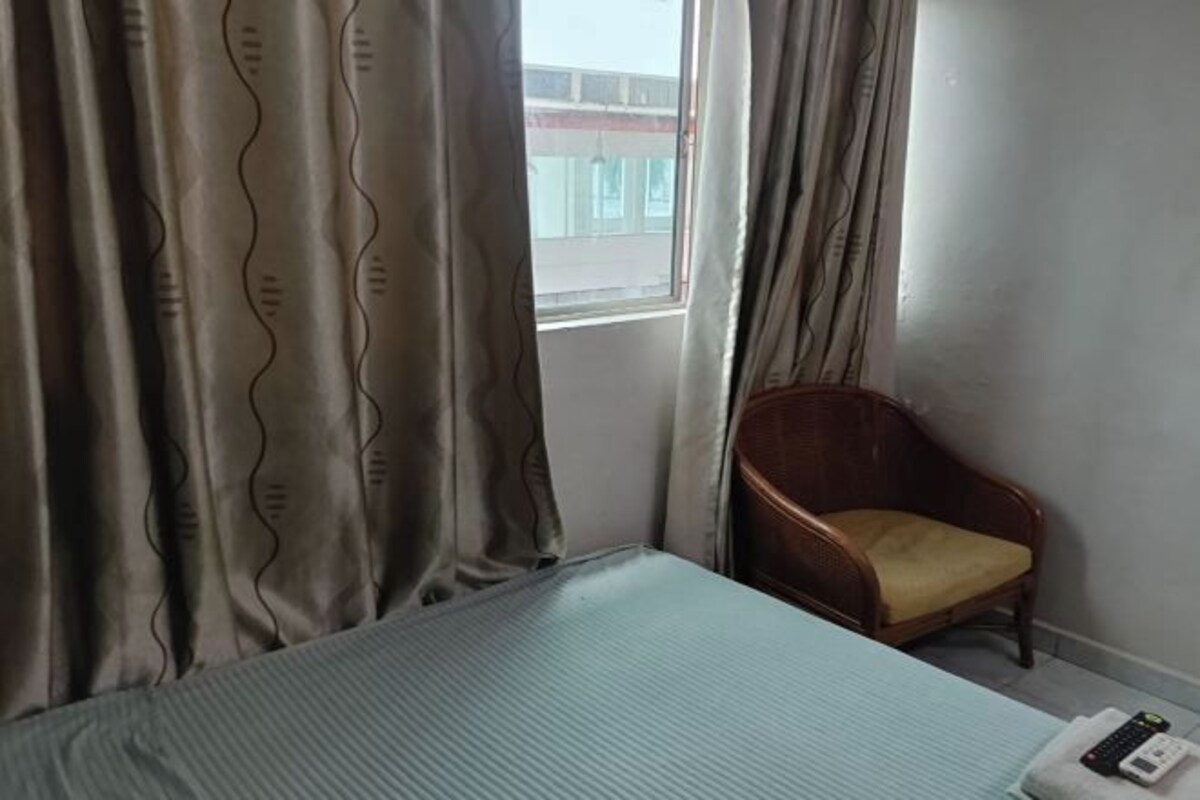 Una habitación de hotel con una cama, una silla y un ventanal con cortinas.