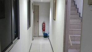 Un pasillo con paredes blancas, suelo de baldosas y una escalera a la derecha.