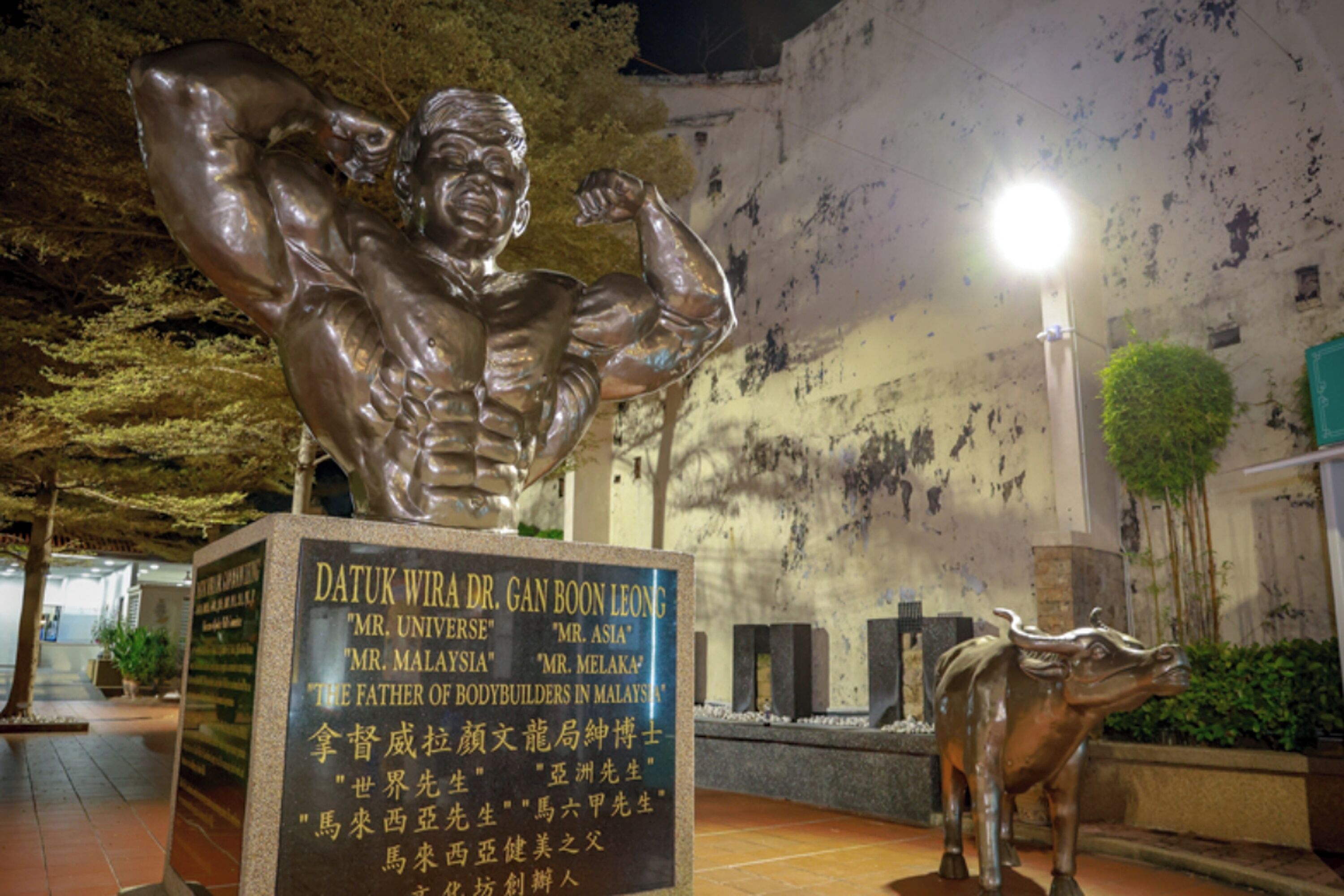 A statue of a muscular man with a plaque in front of a building.