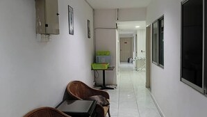 Un pasillo con un comedor que incluye muebles de mimbre y una mesa, una cesta verde sobre una mesita auxiliar y una puerta que da a otra habitación.