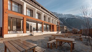 A building with a brick facade, large windows, and outdoor wooden tables and benches. - Mountain House Kazbegi (Kazbegi)