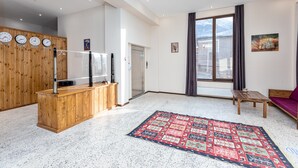A modern living room with a wooden reception desk, a large window with curtains, a red patterned rug, and a painting on the wall. - Mountain House Kazbegi (Kazbegi)