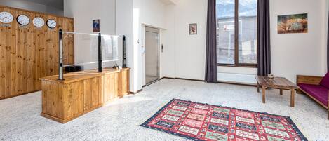 Una sala de estar moderna con un mostrador de recepción de madera, un ventanal con cortinas, una alfombra roja estampada y un cuadro en la pared.