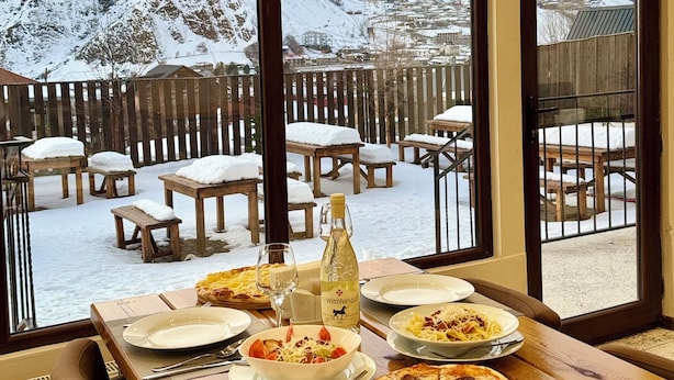 A dining table with plates, glasses, and a bottle, set against a snowy mountain view. - Mountain House Kazbegi (Kazbegi)