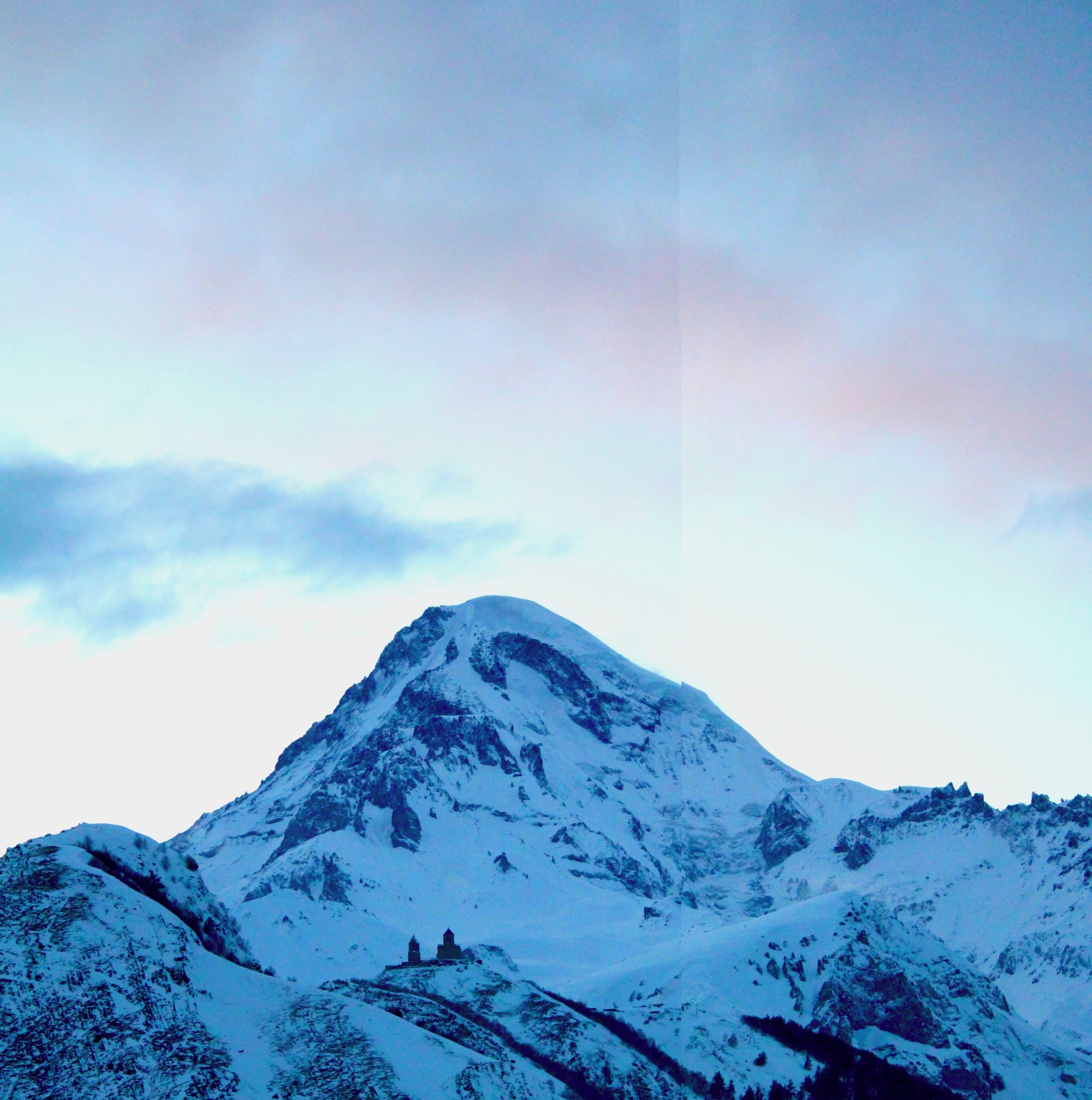Une montagne enneigée, avec un petit bâtiment au sommet.