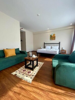 A modern hotel room with a green sofa, a bed with white bedding, a small wooden table, and a patterned rug. - Mountain House Kazbegi (Kazbegi)