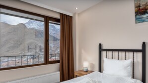 A hotel room with a bed, a nightstand, a lamp, and a window with a mountain view. - Mountain House Kazbegi (Kazbegi)