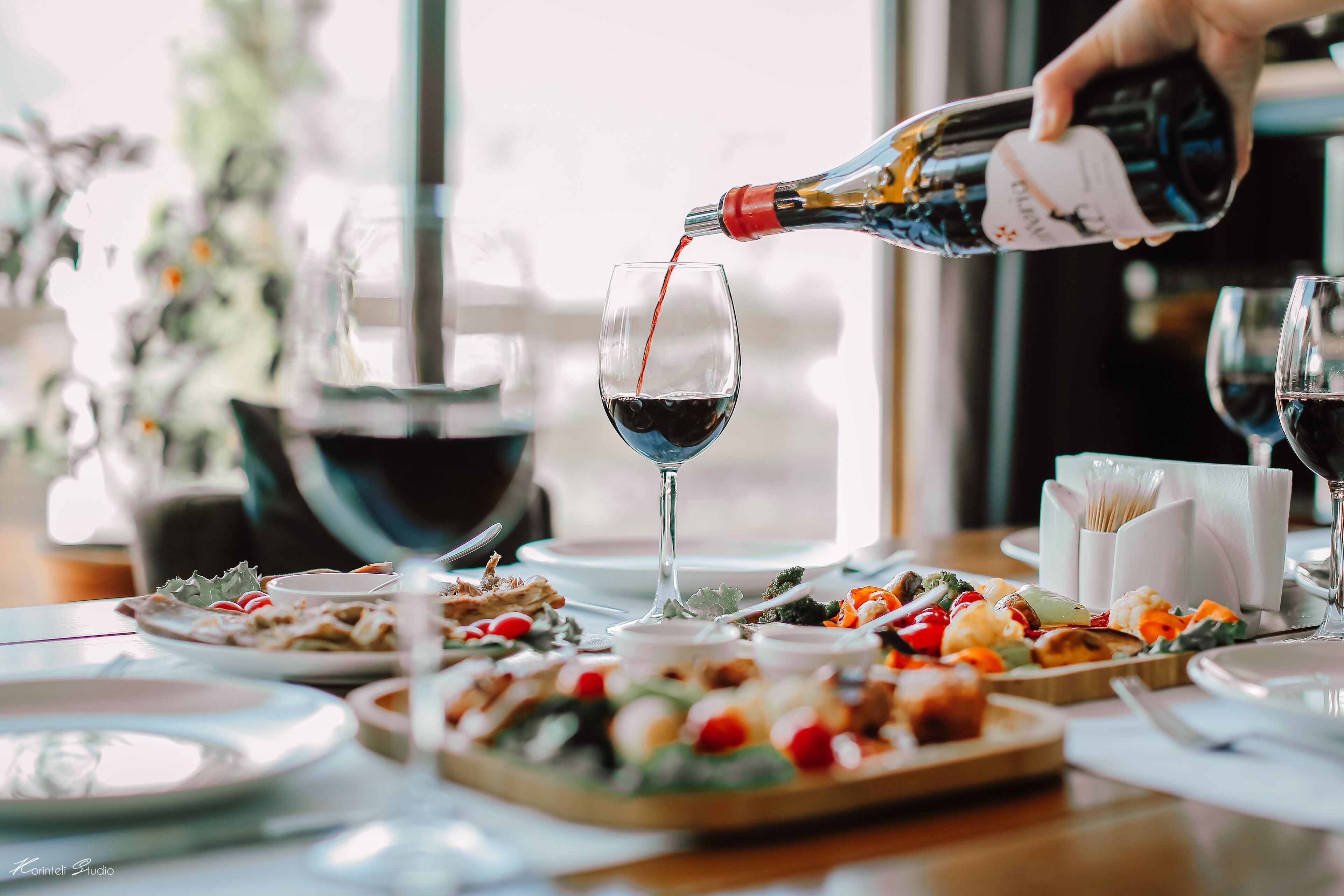 A dining table with various dishes and a bottle of red wine being poured into a glass.