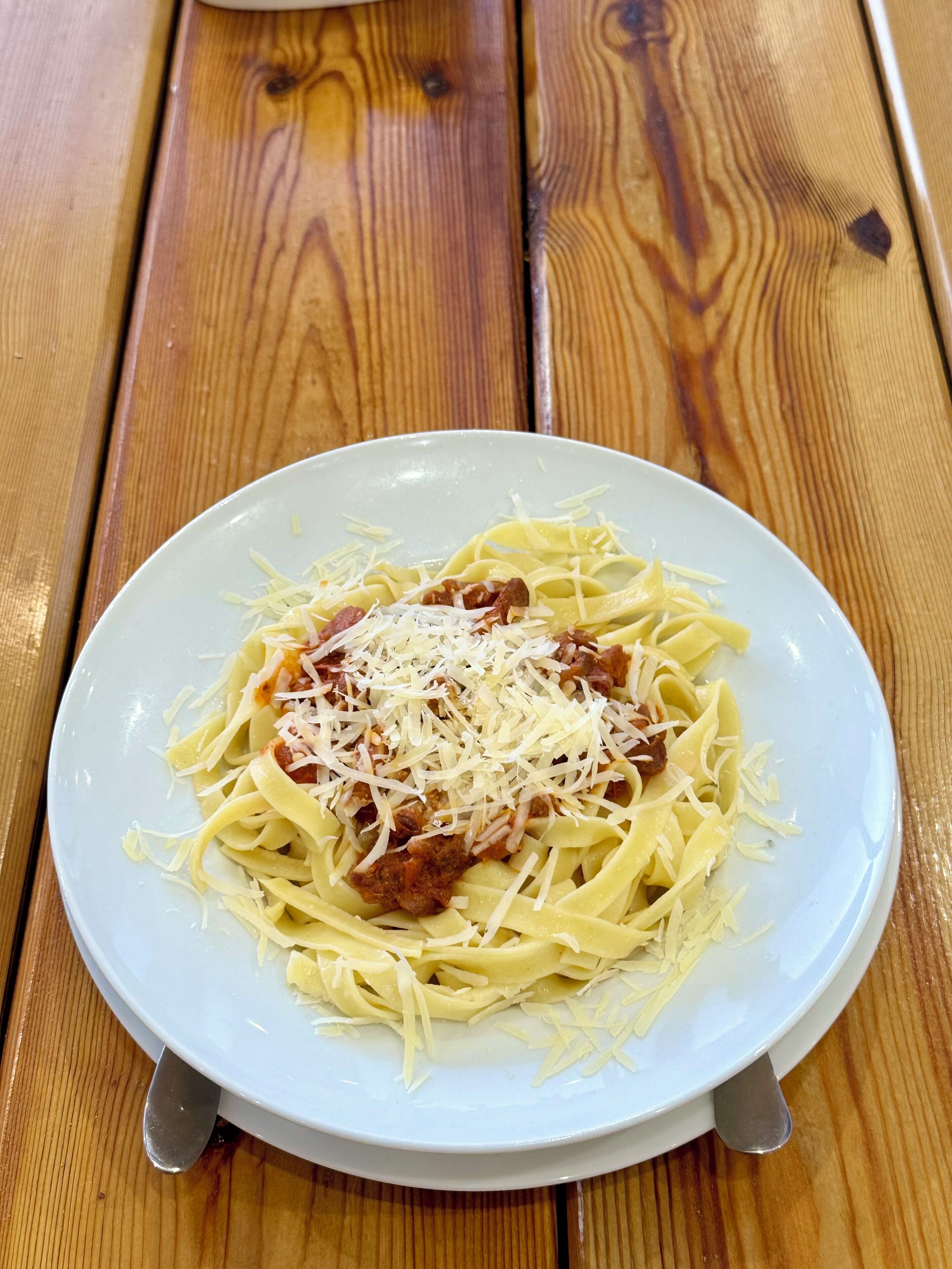 A plate of pasta with meat and cheese on a wooden table.