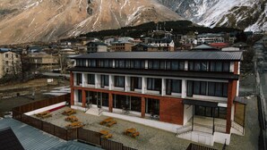 A modern building with a flat roof and multiple windows, surrounded by a parking area with several cars. - Mountain House Kazbegi (Kazbegi)