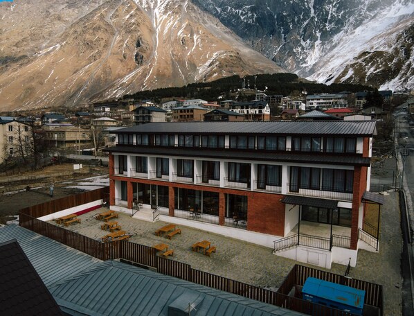 A modern building with a flat roof and multiple windows, surrounded by a parking area with several cars. - Mountain House Kazbegi (Kazbegi)