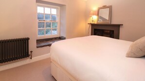 A bedroom with a bed, a window, a fireplace, and a radiator. - Hazelrigg Cottage (Ulverston)