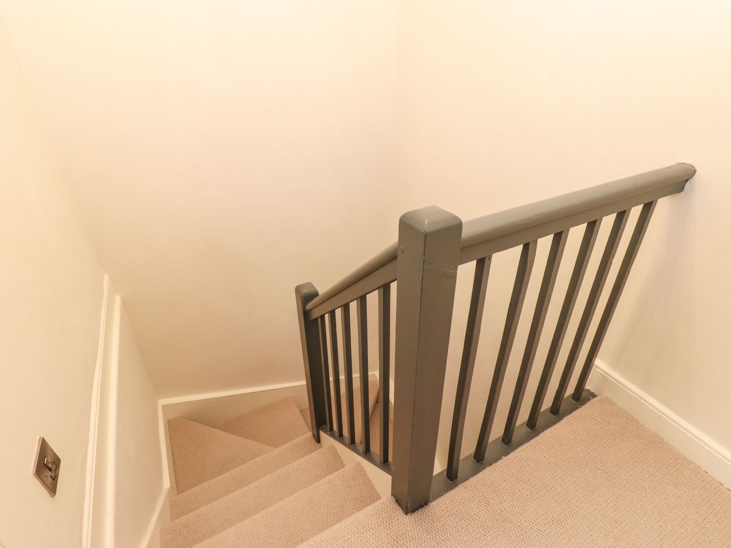 A carpeted staircase with a wooden handrail and a light switch on the wall.