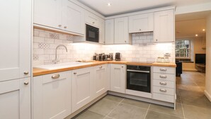 A modern kitchen with white cabinetry, a built-in oven, and a microwave. - Hazelrigg Cottage (Ulverston)