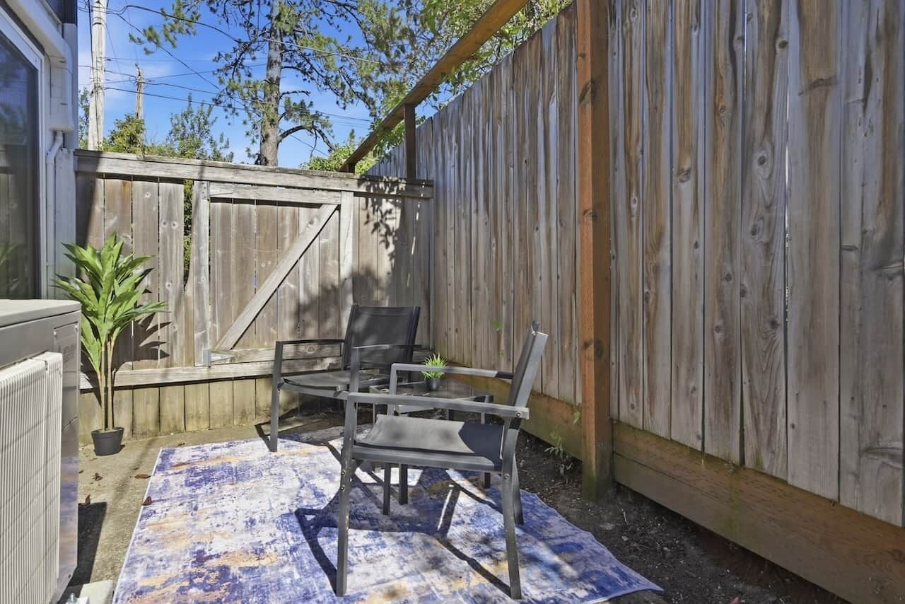Un patio con valla de madera, una mesa, dos sillas y una planta en maceta.