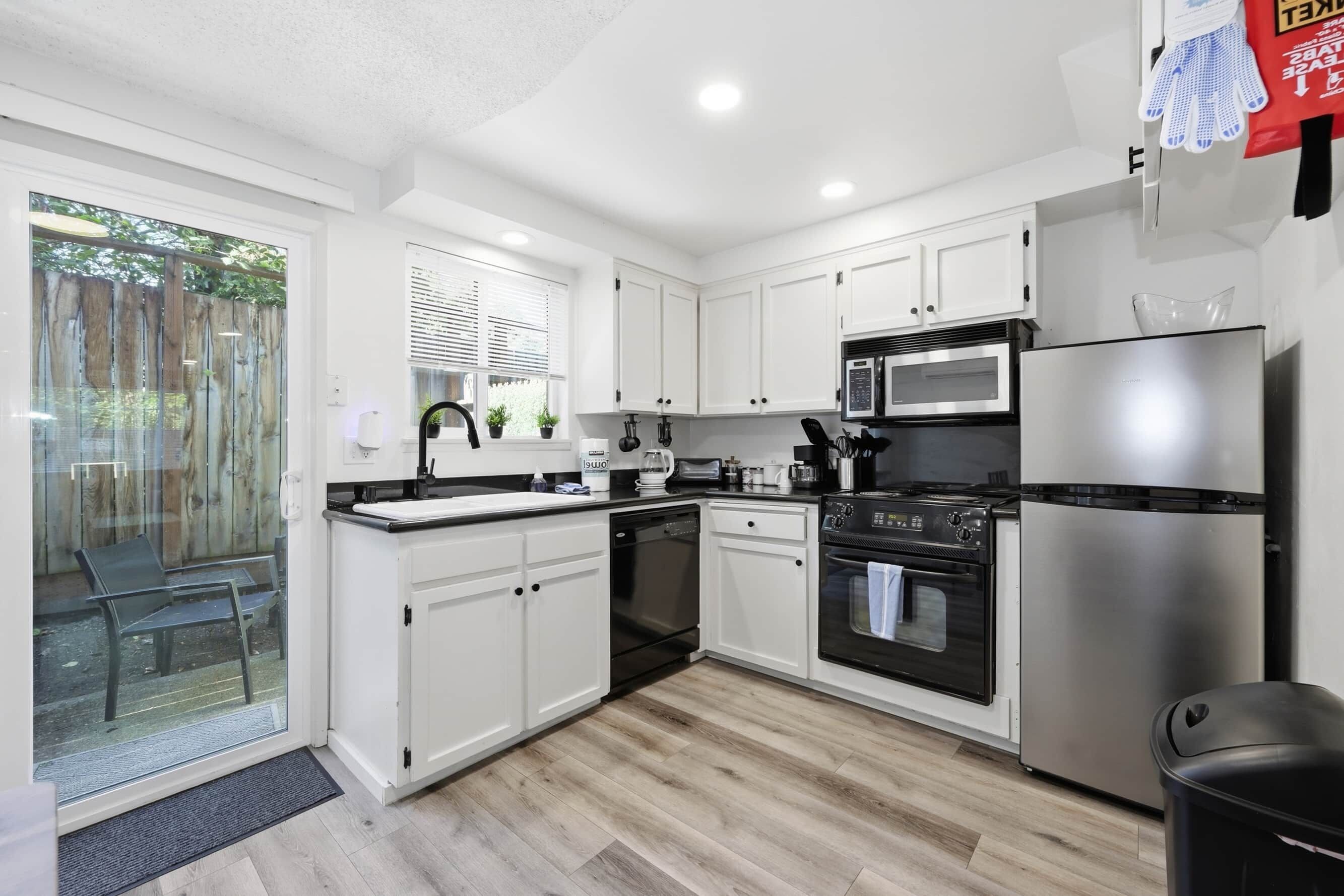 A modern kitchen with white cabinets, stainless steel appliances, and a glass door entrance.