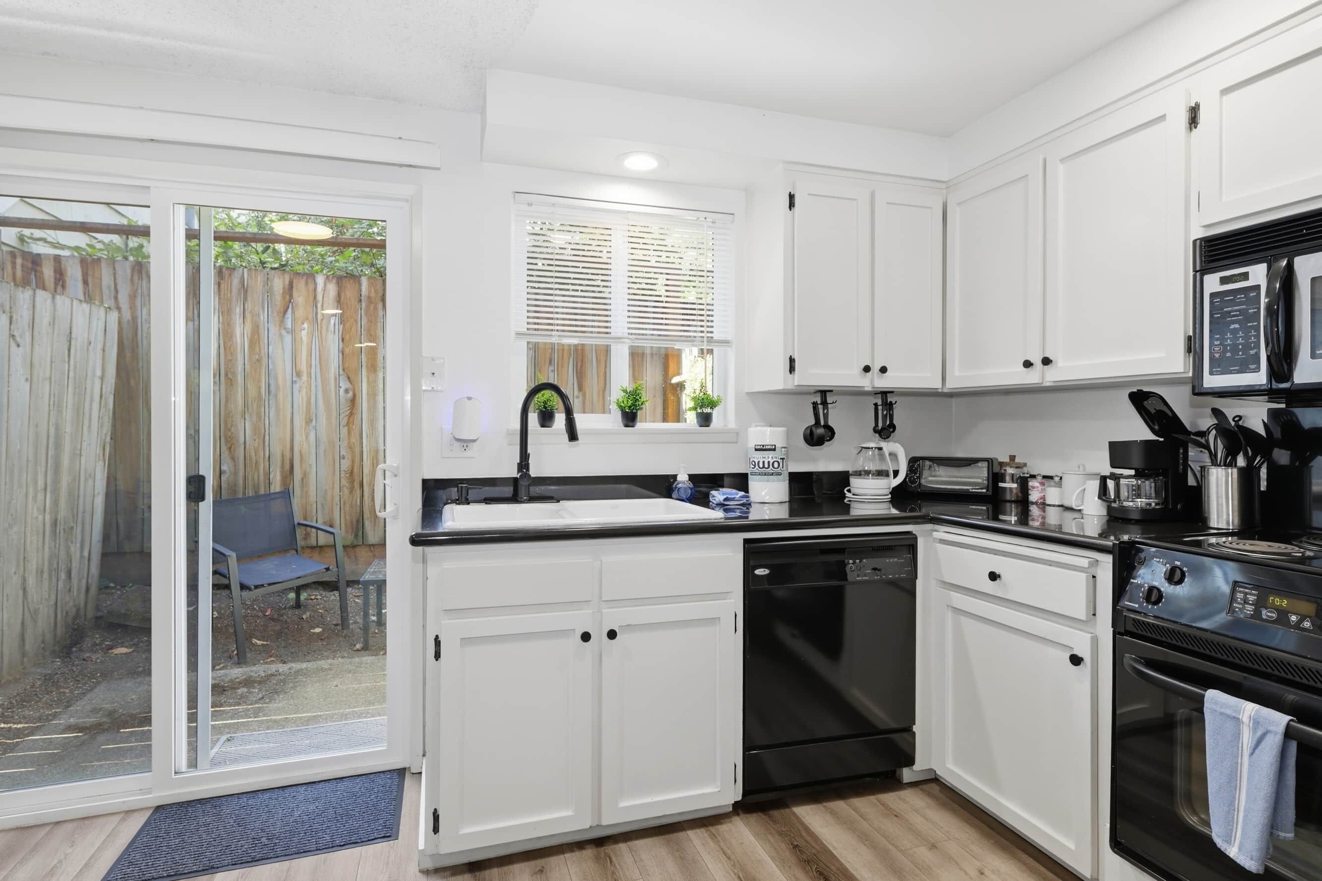 A compact kitchen with white cabinets, a black dishwasher, a microwave, and a stove.