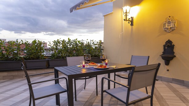 A rooftop terrace with a table set for two, surrounded by chairs, and a potted plant in the background. - Modern apartment in Chiaia on two levels with panoramic terrace (Napoli)