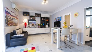 A modern living room with a sofa, a dining table with chairs, a kitchen area, and a large window. - Modern apartment in Chiaia on two levels with panoramic terrace (Napoli)