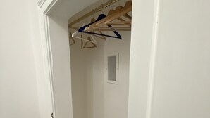 Kapea käytävä, jossa on puinen ovikehys, pieni ikkuna ja vaateteline, jossa on henkareita.