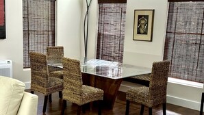 A dining area with a glass-top table surrounded by wicker chairs, a white sofa, and a framed picture on the wall.