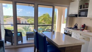 Una cocina moderna con una isla grande, un comedor con mobiliario de mimbre y vistas a un paisaje tropical a través de amplios ventanales correderas.