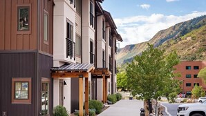A modern multi-story building with a covered walkway, surrounded by greenery and a mountainous backdrop. - Iron Mt Hot Spgs Condo #207 | Mtn Views | Sleeps 4 (Glenwood Springs)