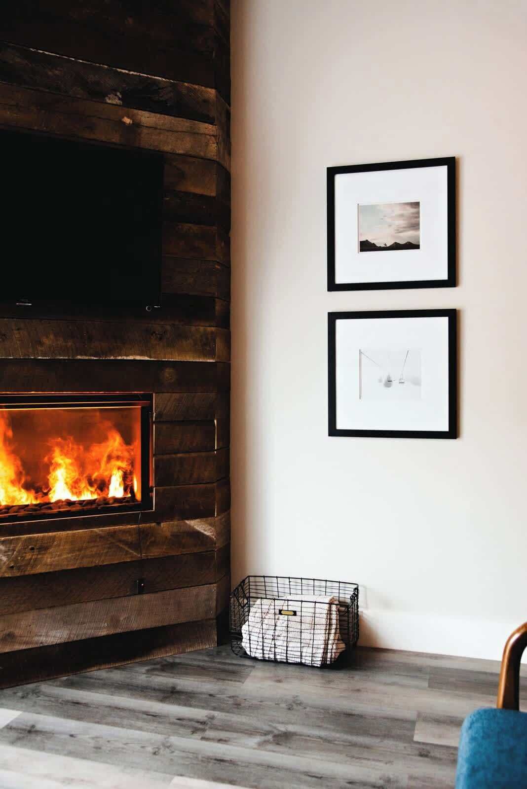 A room with a fireplace, two framed pictures on the wall, and a wire basket on the floor.