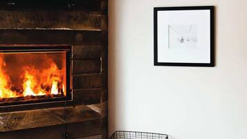 A room with a fireplace, two framed pictures on the wall, and a wire basket on the floor.