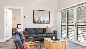 Una sala de estar moderna con un sofá, sillones y una mesa de centro. Hay un ventanal con vistas a un paisaje montañoso.