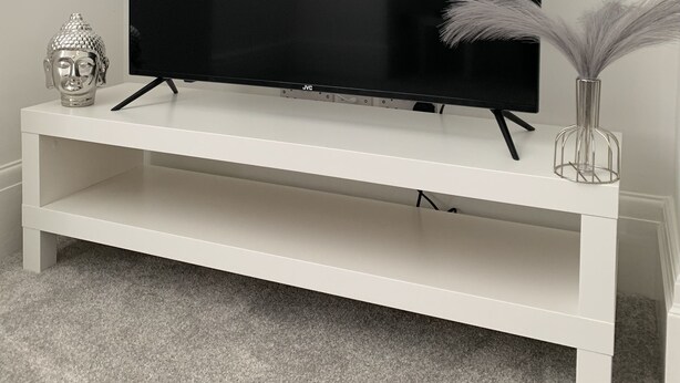 Un televisor de pantalla plana sobre un soporte blanco, mostrando la palabra "NETFLIX" en la pantalla.