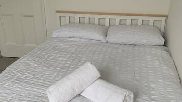 A neatly made bed with a white duvet and pillows, a wooden headboard, and a white door in the background.