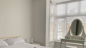 Un dormitorio con cama, cómoda, espejo y ventana con persianas.