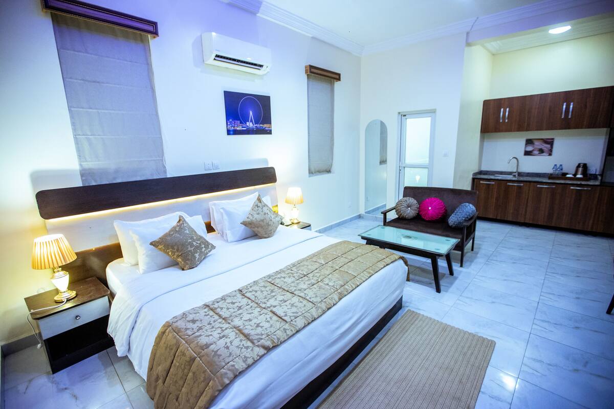 A hotel room with a bed, bedside table, lamp, and a view of the cityscape.