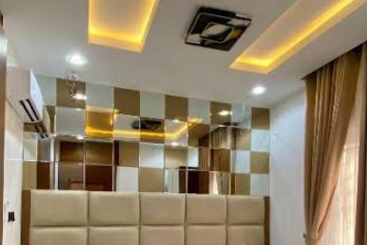 A modern bedroom with a large bed, a headboard with built-in lighting, and a ceiling with recessed lighting.