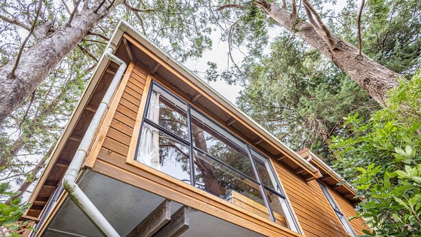 Una cabaña de madera con un ventanal grande, rodeada de árboles.