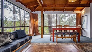 Una habitación acogedora con techo de madera, ventanas amplias, un sofá, una mesa de comedor con sillas y una alfombra estampada.